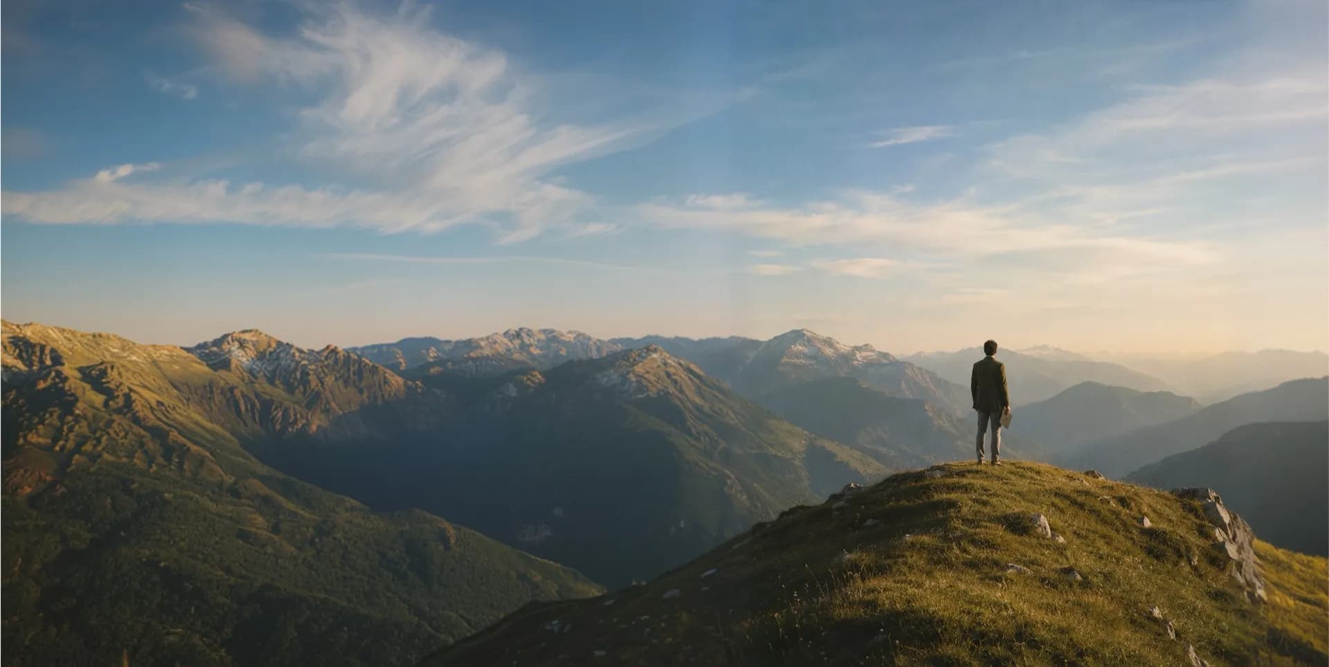 A lone figure on a mountain summit looking out over a vast range at golden hour